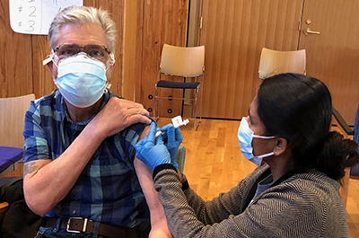 COVID-19 | Fabry Disease News | Jerry receives a dose of the COVID-19 vaccine in a clinic while wearing a face mask and holding up his sleeve.