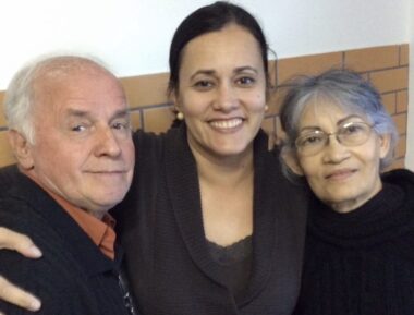 A woman smiles broadly and hugs her mother on the left and her father on the right.