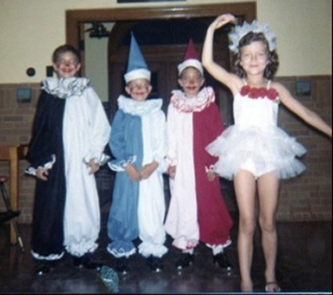 Three boys stand dressed as clowns behind a young girl dressed as a ballerina.